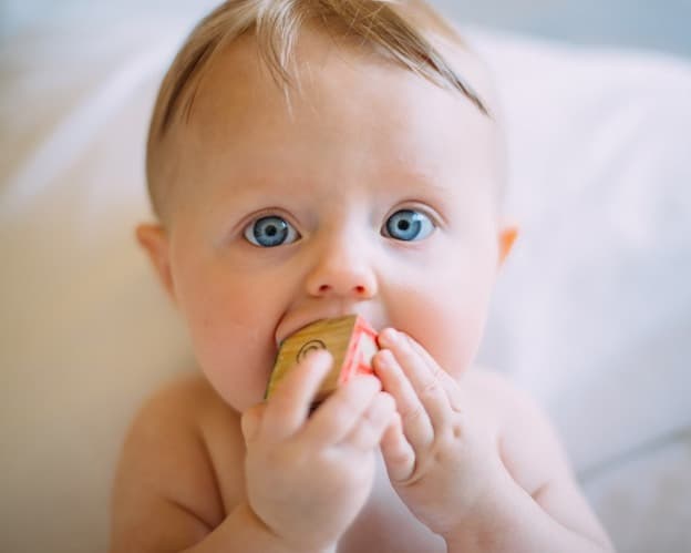 Curious bright blue-eyed baby holding wooden building block