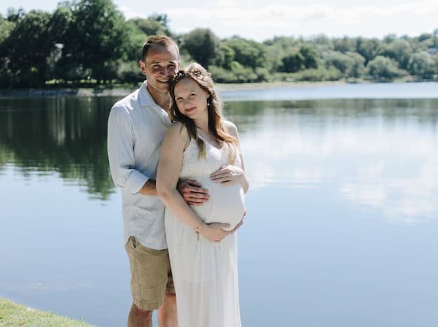 Loving couple embracing near tranquil lake holding baby bump